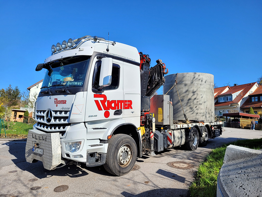 Schwertransport eines Betonblocks mit Lkw-Ladekran in einem Wohngebiet