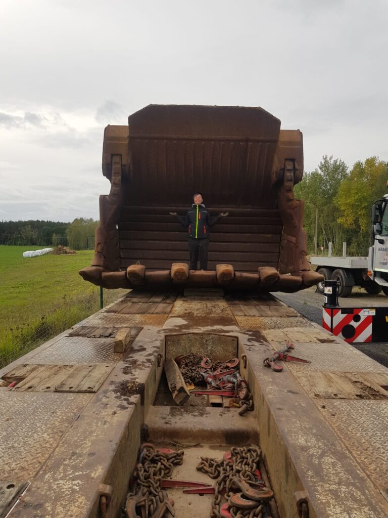 Baggertransport einer überdimensionalen Baggerschaufel auf einem Tieflader mit Person als Größenvergleich