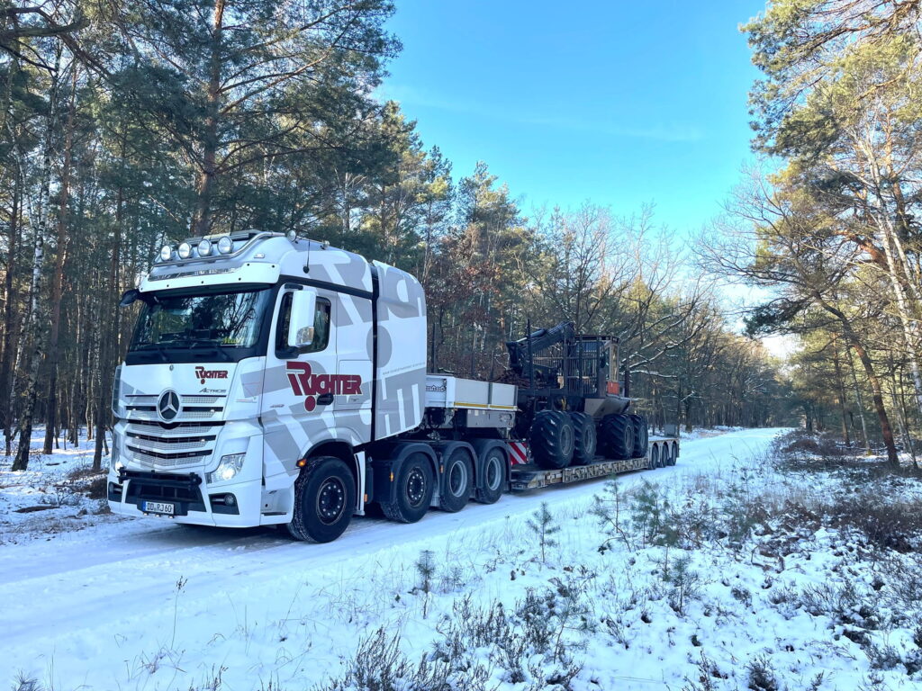 Transport einer Forstmaschine auf einem Tieflader im verschneiten Wald