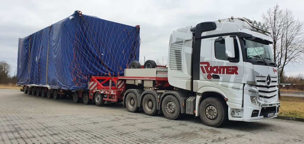 Großraumtransport einer großformatigen, wettergeschützt verpackten Industrieanlage auf einem modularen Schwerlastauflieger