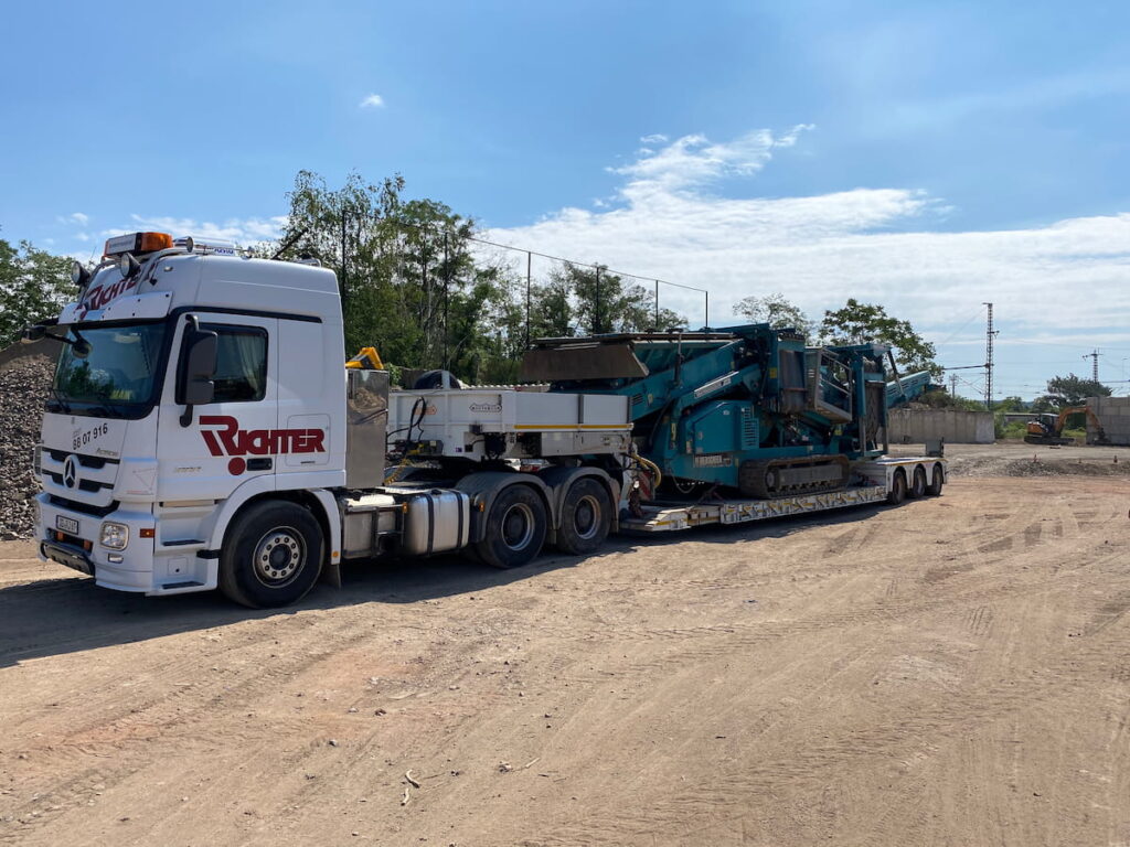 Baumaschinentransport einer mobilen Siebanlage auf einem Tieflader zur Baustelle